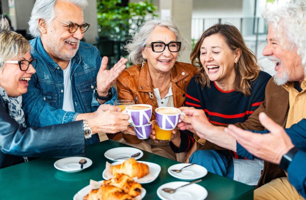  A group of seniors cheers their cups of coffee and orange juice together over a community brunch in assisted living