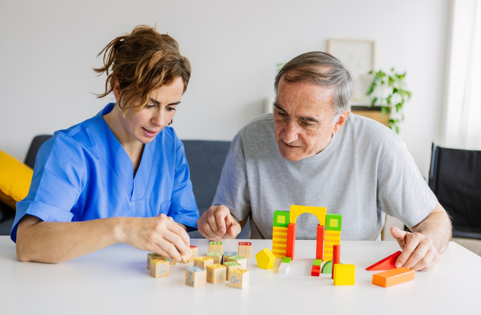 Caregiver and senior playing with blocks, in memory care facility.
